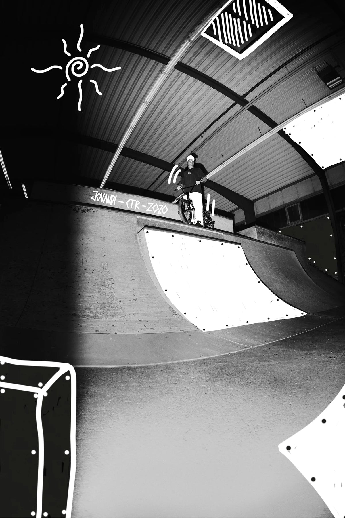 Alt text:
Black-and-white indoor skatepark scene showing a person standing with a BMX bike on a ramp, wearing a **Jovandi T-shirt**. The image features bold white doodle elements, including a sun, accent lines, and graphic overlays on the ramp and ceiling.
