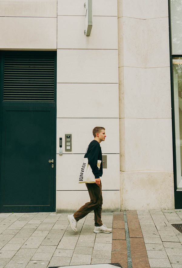 A guy wearing the circle sweater and basic bag in front of a beige wall