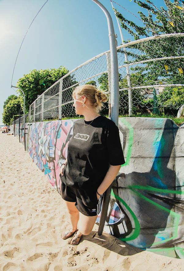 A girl leaning on a graffiti wall on the beach with the bouble tshirt